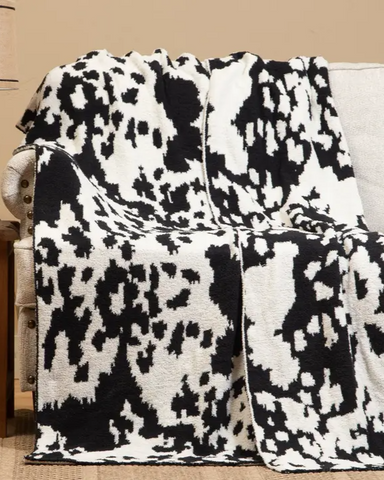 Black and white cowhide patterned blanket draped over a couch in a living room setting.