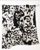 Black and white cowhide patterned blanket draped over a white rod on white background.