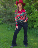 Woman wearing a colorful floral shirt, black jeans, and a red cowboy hat outdoors.