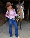 Woman in cowboy hat and pink shirt standing next to a horse in a stable.
