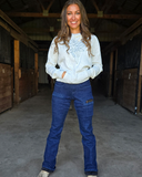 Woman standing in a barn wearing a white sweatshirt and blue jeans.