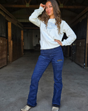 Woman wearing a grey bootstitch sweatshirt and blue jeans in a barn setting