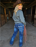 Woman in a cowboy hat and jeans holding a lasso in a stable.