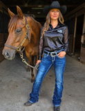 Woman in equestrian attire standing next to a horse in a stable.