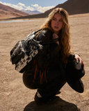 Person squatting in a desert landscape with mountains in the background
