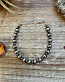 Silver beaded bracelet on a wooden surface with dried flowers.