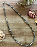 Silver beaded necklace on a wooden surface with dried flowers and an air plant.
