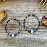 Pair of beaded hoop earrings on a wooden surface with dried leaves.