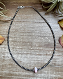 Necklace with a pink bead on a wooden surface