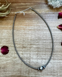 Necklace with beads on a wooden surface with dried leaves and flowers.