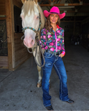 Woman in a pink cowboy hat and colorful shirt standing next to a horse in a barn.