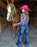 Woman in a pink hat and floral jacket standing next to a horse in a stable.