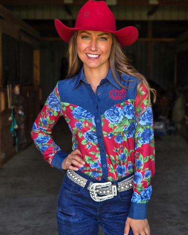 Woman wearing a colorful floral shirt and red cowboy hat in a barn setting