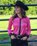 Woman wearing a pink and leopard patterned shirt with a black cowboy hat in an outdoor setting.