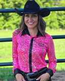 Woman wearing a pink leopard shirt and black cowboy hat in an outdoor setting.