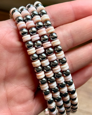 Three beaded necklaces with pink and silver beads laying over a hand.