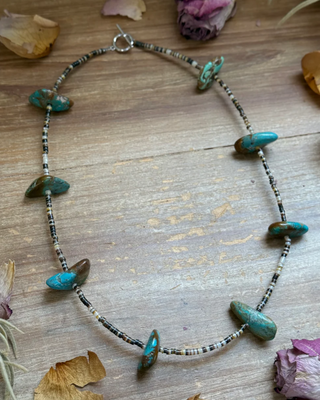 Necklace with turquoise stones on a wooden surface with dried leaves and flowers.