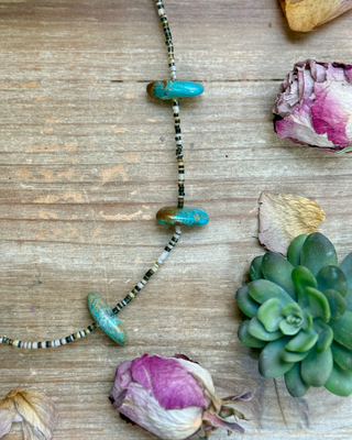 Necklace with turquoise and black beads on a wooden surface with dried flowers and succulents.