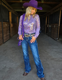 Person wearing a purple cowboy hat, purple top, and blue jeans in a barn setting.