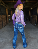 Woman wearing a purple cowboy hat and shirt with blue jeans in a barn setting