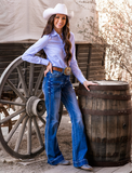 A girl modeling the Dare Me Trouser Jeans. She has one hand on her hip and the other placed on a barrel that is next to her. There is a wagon behind her.