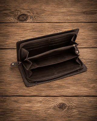 An open black leather wallet with multiple card slots and a zip compartment, displayed on a rustic wooden surface.