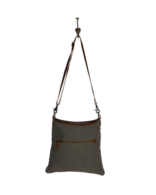 A dark gray canvas shoulder bag with brown leather trim and a matching adjustable shoulder strap, hanging against a plain white background.