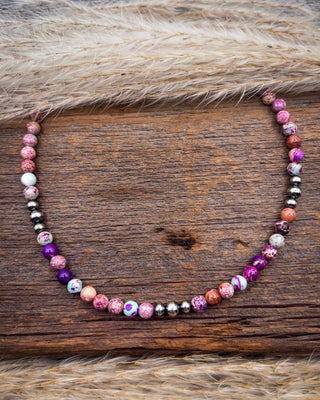 A beaded necklace with marbled pink, purple, white, and brown beads, displayed on a rustic wooden surface with a faux fur trim.