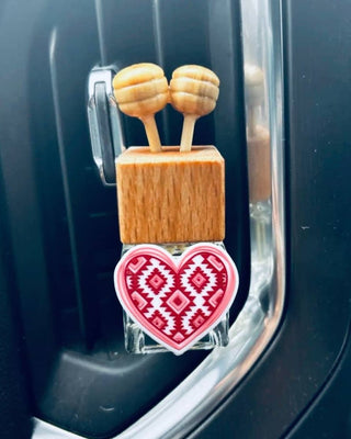 A car air freshener or decorative plug featuring a light wood block with two honeycomb-shaped wooden tops and a red and white patterned heart charm, inserted into a black car door slot.