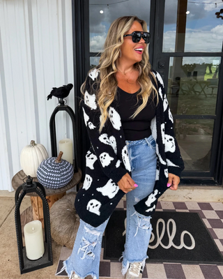Woman wearing a black cardigan with white ghost patterns on a porch decorated for Halloween.