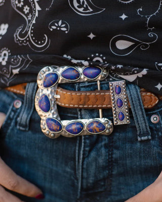 Close-up of a person wearing a belt with a decorative buckle featuring blue stones and brown leather.