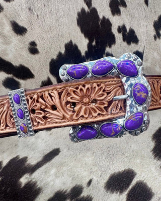 Decorative belt buckle with purple stones on a cowhide background