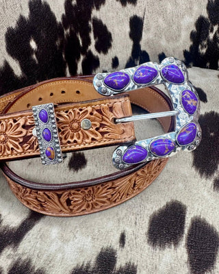Brown leather belt with purple gemstone buckle on a cowhide background