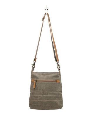 A gray textured canvas shoulder bag with tan leather trim and a matching adjustable shoulder strap, hanging against a plain white background.
