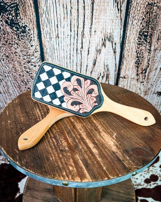 Two hair brushes with wooden handles are crossed on a rustic round wooden stool. 