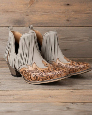 Pair of beige cowboy boots with brown leather detailing on a white background