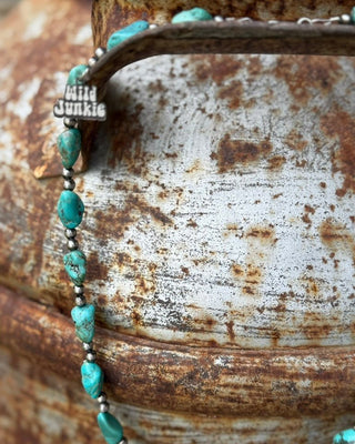 Necklace with turquoise beads and 'Wild Junkie' clasp on a rusty metal surface