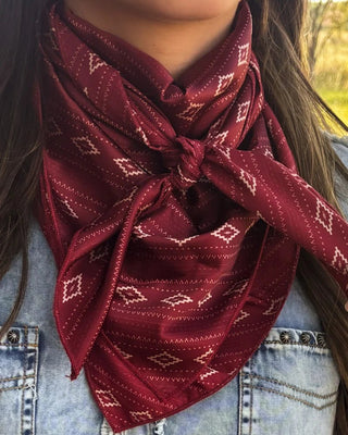 A close-up of a person wearing a deep red neck scarf with a white geometric diamond pattern, tied in a knot at the collarbone over a light blue denim jacket.