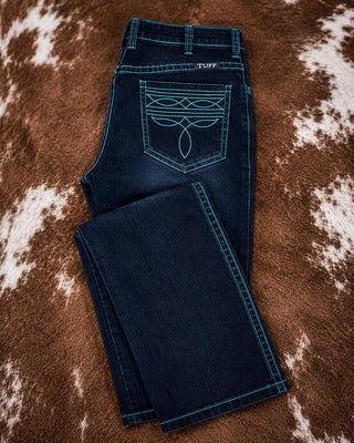 A pair of dark blue denim jeans laid flat on a brown and white cowhide rug. The back pocket features a large turquoise embroidered graphic, and the brand name 'TUFF' is visible on the waistband.