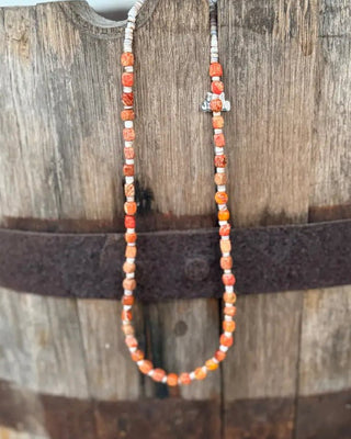 A beaded necklace with orange, white, and brown marbled beads draped over a rustic wooden barrel.