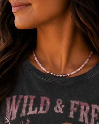 A close-up of a woman wearing a dark gray graphic t-shirt with a western design featuring a bull skull, cacti, and the text 'WILD & FREE' and 'STAY TRUE WESTERN SOUL'.