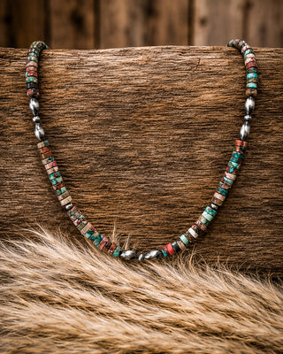 A beaded necklace with small turquoise, red, brown, and silver beads draped over a rustic wooden log with fur in the foreground.