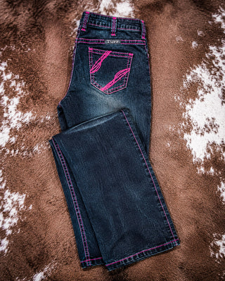 A pair of dark blue denim jeans with bright pink contrast stitching and a matching pink embroidered back pocket design, laid flat on a brown and white cowhide rug.