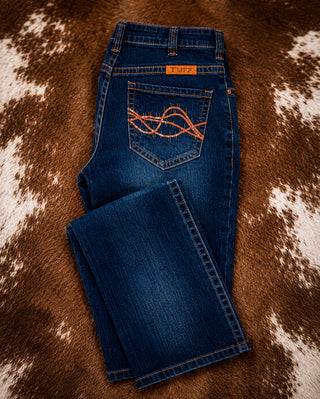 A pair of blue denim jeans laid flat on a brown and white cowhide rug. The back pocket features distinctive orange embroidery, and an orange 'TRUCK' brand label is visible at the waistband.