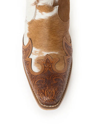 A close-up top-down view of a western boot featuring a brown and white cowhide upper with intricate hand-tooled floral leather detailing on the pointed toe.