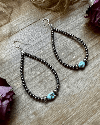 Pair of beaded earrings with turquoise stones on a wooden surface with dried flowers.