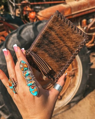 Hand holding a brown leather wallet with vintage tractor in the background