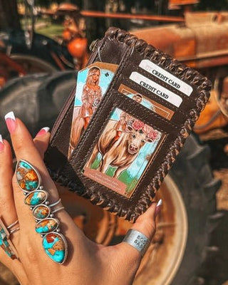 Hand holding a leather wallet with cards, surrounded by rustic outdoor elements.
