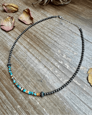 Necklace with colorful beads on a wooden surface with dried leaves and an air plant.