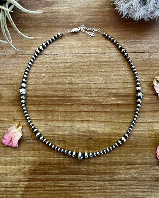 Necklace with black and silver beads on a wooden surface with dried flowers and plants.
